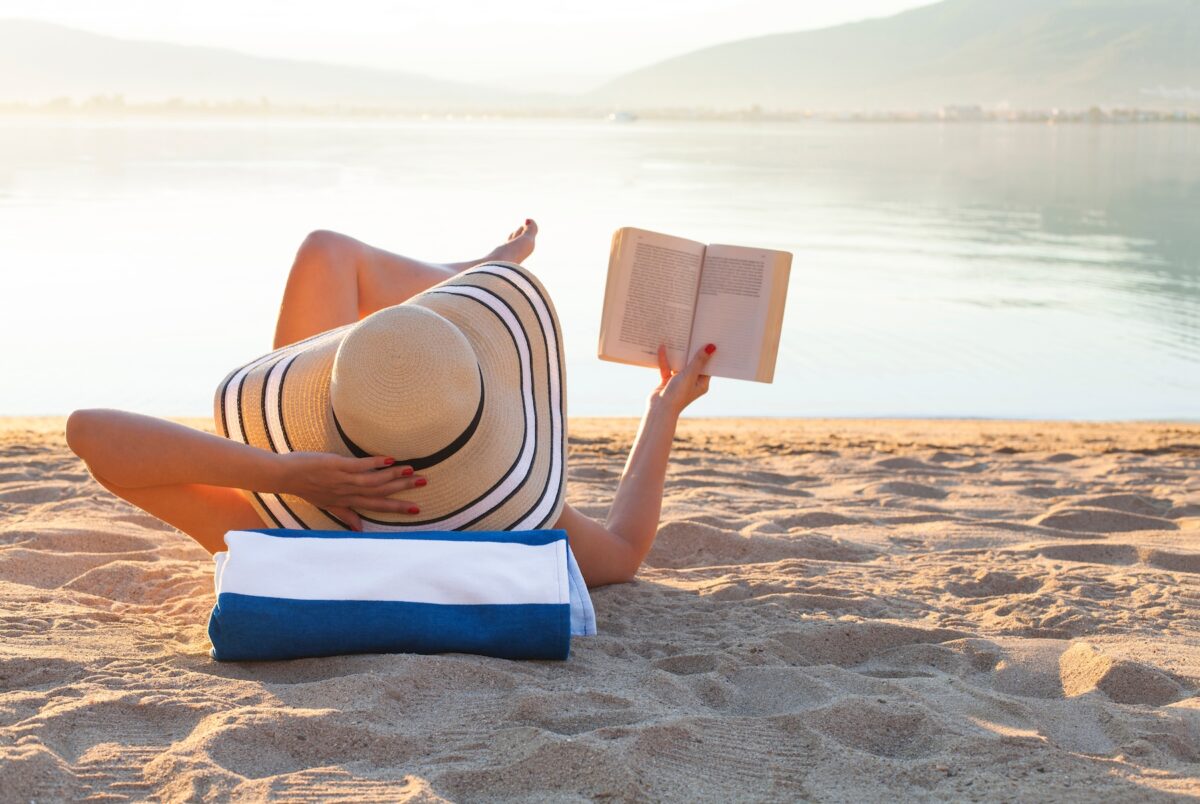 Young woman relaxing on the beach, reading a book